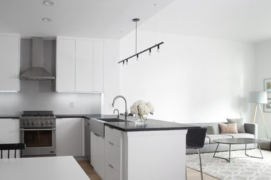 Large minimalist u-shaped light wood floor open concept kitchen photo in New York with a farmhouse sink, flat-panel cabinets, white cabinets, limestone countertops, gray backsplash, porcelain backsplash, stainless steel appliances and an island