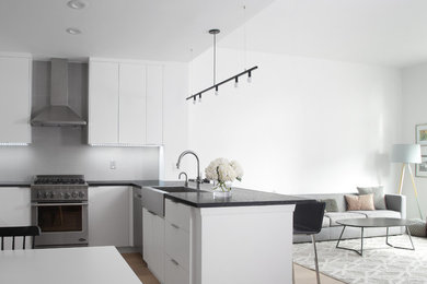 Inspiration for a large modern u-shaped open plan kitchen in New York with a belfast sink, flat-panel cabinets, white cabinets, limestone worktops, grey splashback, porcelain splashback, stainless steel appliances, light hardwood flooring and an island.