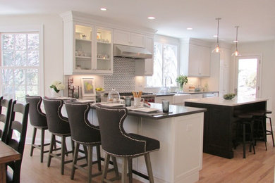 Photo of a large classic l-shaped kitchen in New York with a belfast sink, shaker cabinets, white cabinets, stainless steel appliances, light hardwood flooring, an island and brown floors.