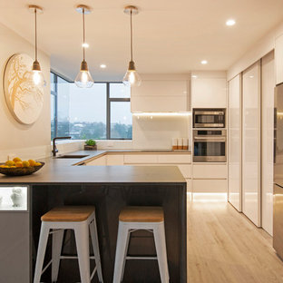 Inspiration for a mid-sized contemporary u-shaped eat-in kitchen in Auckland with an undermount sink, white cabinets, concrete benchtops, white splashback, glass sheet splashback, stainless steel appliances, cork floors, no island, grey floor and grey benchtop.