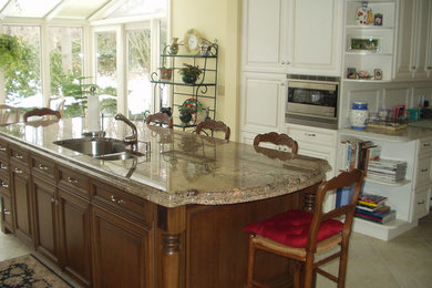 Photo of a large traditional u-shaped kitchen/diner in New York with a submerged sink, raised-panel cabinets, white cabinets, granite worktops, beige splashback, ceramic splashback, stainless steel appliances, ceramic flooring, an island and beige floors.