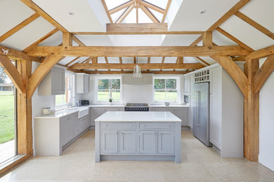 Inspiration for a large traditional u-shaped kitchen/diner in Surrey with a double-bowl sink, shaker cabinets, grey cabinets, composite countertops, white splashback, porcelain splashback, stainless steel appliances, travertine flooring, an island, beige floors and white worktops.