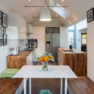 This is an example of a small contemporary u-shaped kitchen/diner in Hertfordshire with a double-bowl sink, wood worktops, white splashback, ceramic splashback, stainless steel appliances, ceramic flooring, grey floors, brown worktops, flat-panel cabinets, white cabinets and no island.