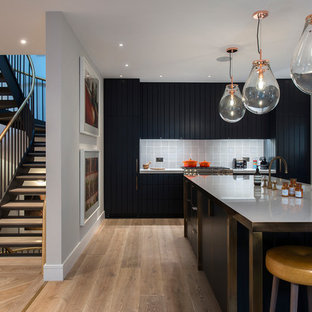 Photo of a modern l-shaped kitchen in London with light hardwood flooring, an island, beige floors, flat-panel cabinets, black cabinets, stainless steel worktops, grey splashback, ceramic splashback, integrated appliances and grey worktops.