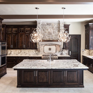 Photo of a large mediterranean u-shaped open plan kitchen in Sacramento with an undermount sink, raised-panel cabinets, dark wood cabinets, granite benchtops, multi-coloured splashback, stone slab splashback, stainless steel appliances, travertine floors, with island and beige floor.