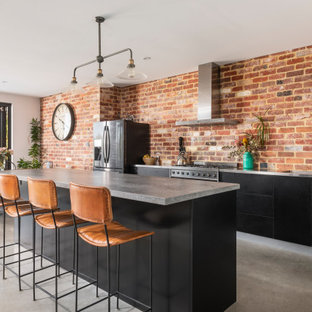 Mid-sized industrial galley open plan kitchen in Perth with an undermount sink, flat-panel cabinets, black cabinets, concrete benchtops, red splashback, brick splashback, stainless steel appliances, concrete floors, with island, grey floor and grey benchtop.