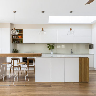 Large minimalist l-shaped medium tone wood floor and brown floor open concept kitchen photo in Sydney with an undermount sink, flat-panel cabinets, white cabinets, glass sheet backsplash, stainless steel appliances, an island, quartz countertops, white backsplash and white countertops
