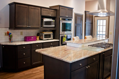Inspiration for a large transitional galley laminate floor and brown floor enclosed kitchen remodel in Denver with a double-bowl sink, shaker cabinets, dark wood cabinets, granite countertops, white backsplash, subway tile backsplash, stainless steel appliances, an island and multicolored countertops