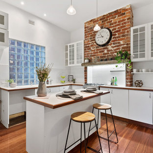 Mid-sized country l-shaped kitchen in Perth with flat-panel cabinets, white cabinets, glass tile splashback, medium hardwood floors, brown floor, white benchtop, a double-bowl sink, wood benchtops, white splashback and with island.