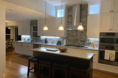 Example of a mid-sized transitional galley medium tone wood floor and multicolored floor eat-in kitchen design in Cincinnati with flat-panel cabinets, white cabinets, granite countertops, gray backsplash, stone tile backsplash, stainless steel appliances, an island and gray countertops
