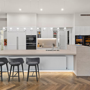 Inspiration for a large contemporary galley open plan kitchen in Melbourne with an undermount sink, recessed-panel cabinets, white cabinets, grey splashback, panelled appliances, medium hardwood floors, with island, brown floor, beige benchtop, granite benchtops and granite splashback.