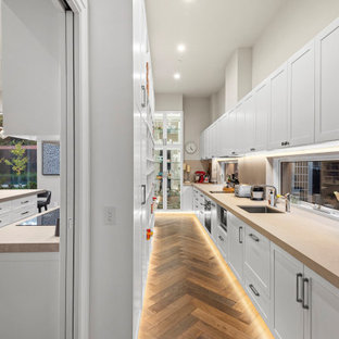 Photo of a large contemporary galley kitchen pantry in Melbourne with a single-bowl sink, recessed-panel cabinets, white cabinets, window splashback, stainless steel appliances, medium hardwood floors, no island, brown floor, beige benchtop and granite benchtops.