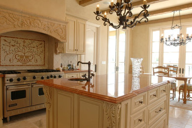 Inspiration for a mid-sized mediterranean u-shaped limestone floor enclosed kitchen remodel in Orange County with a double-bowl sink, raised-panel cabinets, distressed cabinets, granite countertops, beige backsplash, stone tile backsplash, stainless steel appliances and an island