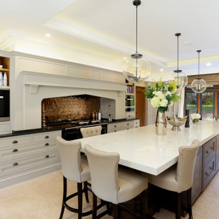 This is an example of a large classic galley kitchen in Kent with recessed-panel cabinets, an island, white cabinets, metallic splashback, black appliances, beige floors and black worktops.