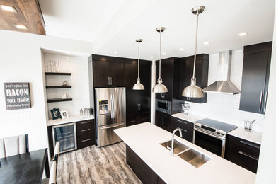Moderne Wohnküche in L-Form mit Küchenrückwand in Weiß, Rückwand aus Keramikfliesen, Küchengeräten aus Edelstahl, Laminat, Kücheninsel, flächenbündigen Schrankfronten, dunklen Holzschränken, Quarzit-Arbeitsplatte und grauem Boden in Calgary