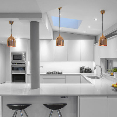 Eat-in kitchen - mid-sized contemporary u-shaped ceramic tile eat-in kitchen idea in Dublin with an integrated sink, shaker cabinets, white cabinets, solid surface countertops, white backsplash, paneled appliances and a peninsula