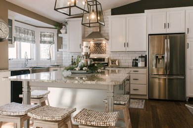 Inspiration for a mid-sized timeless l-shaped brown floor and dark wood floor eat-in kitchen remodel in Other with a farmhouse sink, white cabinets, white backsplash, stainless steel appliances, an island, recessed-panel cabinets, granite countertops and ceramic backsplash