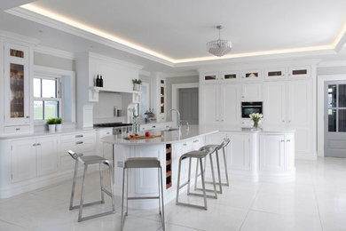 Large classic l-shaped open plan kitchen in Belfast with a submerged sink, beaded cabinets, white cabinets, quartz worktops, grey splashback, stone slab splashback, stainless steel appliances, porcelain flooring, an island and grey floors.