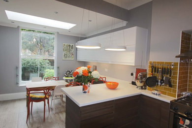 This is an example of a medium sized contemporary u-shaped kitchen/diner in Hertfordshire with dark wood cabinets, ceramic splashback, integrated appliances, porcelain flooring and a breakfast bar.