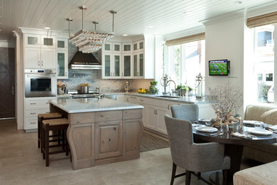 Example of a beach style eat-in kitchen design in Orange County with a double-bowl sink, glass-front cabinets, white cabinets, multicolored backsplash, mosaic tile backsplash, stainless steel appliances and an island