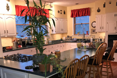ボストンにある高級な広いカントリー風のおしゃれなアイランドキッチン (ドロップインシンク、レイズドパネル扉のキャビネット、白いキャビネット、ベージュキッチンパネル、ガラス板のキッチンパネル、黒い調理設備、ベージュの床、ベージュのキッチンカウンター) の写真