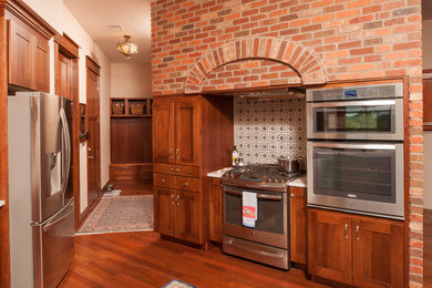 Inredning av ett amerikanskt avskilt, stort u-kök, med en undermonterad diskho, skåp i shakerstil, skåp i mellenmörkt trä, bänkskiva i kvarts, rostfria vitvaror, mellanmörkt trägolv, en halv köksö och brunt golv