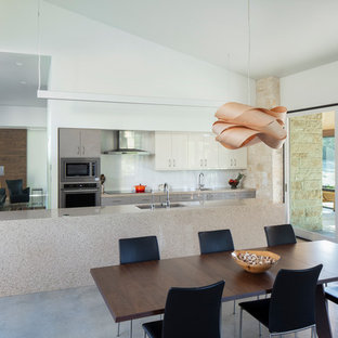 Idée de décoration pour une cuisine américaine vintage avec un évier encastré, un placard à porte plane, des portes de placard grises, une crédence blanche, une crédence en feuille de verre, un électroménager en acier inoxydable, béton au sol, un îlot central, un sol gris et un plan de travail gris.