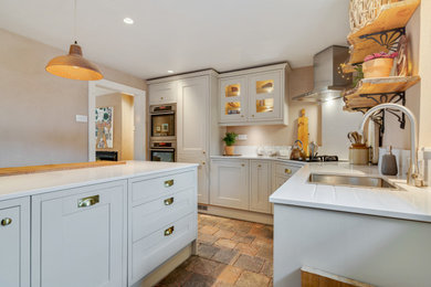 Small traditional u-shaped enclosed kitchen in Cheshire with a submerged sink, shaker cabinets, green cabinets, engineered stone countertops, white splashback, engineered quartz splashback, stainless steel appliances, brick flooring, a breakfast bar, multi-coloured floors and white worktops.