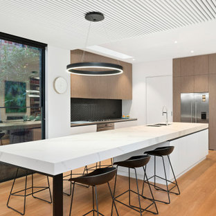 Design ideas for a contemporary u-shaped kitchen in Melbourne with an undermount sink, flat-panel cabinets, medium wood cabinets, black splashback, stainless steel appliances, medium hardwood floors, with island, brown floor and grey benchtop.