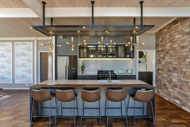 This is an example of a medium sized contemporary galley kitchen/diner in Hamilton with a submerged sink, flat-panel cabinets, dark wood cabinets, engineered stone countertops, white splashback, stone slab splashback, black appliances, light hardwood flooring, an island, brown floors and white worktops.