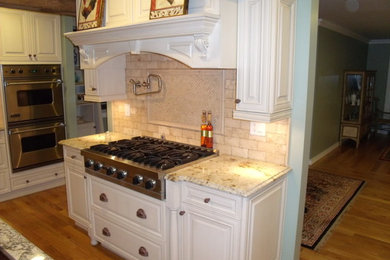 Inspiration for a mid-sized transitional u-shaped medium tone wood floor eat-in kitchen remodel in New York with a farmhouse sink, raised-panel cabinets, white cabinets, granite countertops, beige backsplash, terra-cotta backsplash, stainless steel appliances and an island