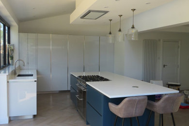 Inspiration for a large contemporary l-shaped open plan kitchen in Essex with an integrated sink, flat-panel cabinets, blue cabinets, quartz worktops, white splashback, stainless steel appliances, light hardwood flooring, an island, beige floors and white worktops.