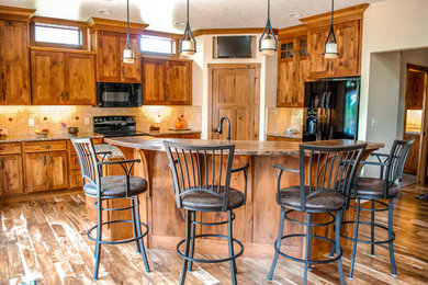 Mid-sized arts and crafts l-shaped medium tone wood floor and brown floor open concept kitchen photo in Minneapolis with shaker cabinets, medium tone wood cabinets, granite countertops, beige backsplash, stone tile backsplash, black appliances, an island and an undermount sink