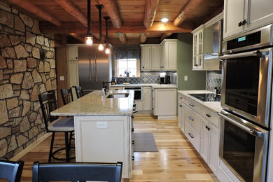 This is an example of a large rustic l-shaped kitchen/diner in New York with a submerged sink, recessed-panel cabinets, white cabinets, granite worktops, grey splashback, porcelain splashback, stainless steel appliances, light hardwood flooring and an island.