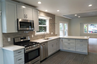 Example of a mid-sized transitional l-shaped ceramic tile and gray floor eat-in kitchen design in San Francisco with an undermount sink, white cabinets, quartz countertops, gray backsplash, subway tile backsplash, stainless steel appliances and recessed-panel cabinets
