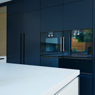 Large contemporary l-shaped eat-in kitchen in London with an integrated sink, flat-panel cabinets, white cabinets, solid surface benchtops, metallic splashback, panelled appliances, ceramic floors and with island.