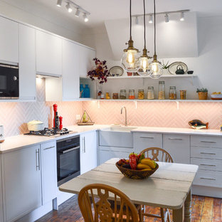 Photo of a contemporary l-shaped kitchen/diner in London with a belfast sink, raised-panel cabinets, white cabinets, pink splashback, integrated appliances, medium hardwood flooring, no island, brown floors and white worktops.