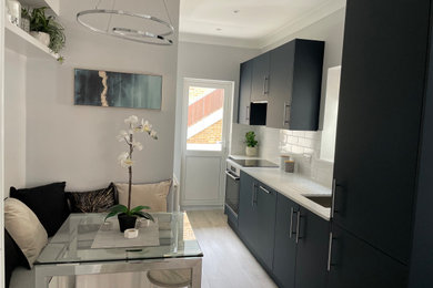 Small contemporary galley open plan kitchen with a built-in sink, flat-panel cabinets, grey cabinets, composite countertops, white splashback, porcelain splashback, integrated appliances, laminate floors, grey floors and white worktops.