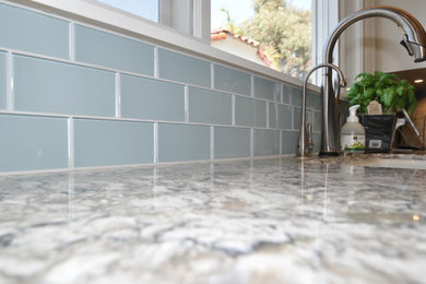 Inspiration for a mid-sized timeless l-shaped porcelain tile enclosed kitchen remodel in Los Angeles with a farmhouse sink, shaker cabinets, white cabinets, blue backsplash, glass tile backsplash, stainless steel appliances and no island