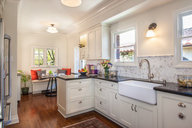 Mid-sized trendy u-shaped medium tone wood floor and brown floor enclosed kitchen photo in Los Angeles with a farmhouse sink, shaker cabinets, white cabinets, granite countertops, white backsplash, ceramic backsplash, stainless steel appliances and no island