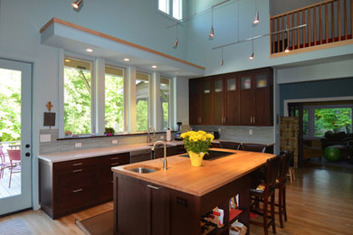 Example of a mid-sized trendy l-shaped medium tone wood floor and brown floor eat-in kitchen design in Charlotte with a farmhouse sink, shaker cabinets, dark wood cabinets, gray backsplash, stainless steel appliances and an island