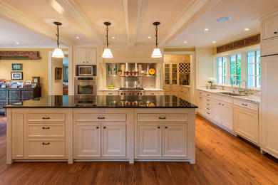 Photo of a large traditional l-shaped kitchen/diner in Minneapolis with flat-panel cabinets, granite worktops, light hardwood flooring and an island.