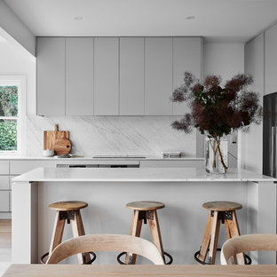 Inspiration for a large contemporary u-shaped eat-in kitchen in Wollongong with grey cabinets, marble benchtops, marble splashback, stainless steel appliances, with island, flat-panel cabinets, white splashback, medium hardwood floors, brown floor, white benchtop and a double-bowl sink.