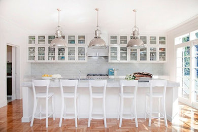 Klassisk inredning av ett mellanstort kök, med en undermonterad diskho, luckor med glaspanel, vita skåp, marmorbänkskiva, grått stänkskydd, stänkskydd i glaskakel, rostfria vitvaror, mellanmörkt trägolv och en köksö