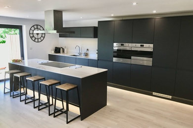 Large contemporary single-wall open plan kitchen in Buckinghamshire with a single-bowl sink, flat-panel cabinets, grey cabinets, quartz worktops, stainless steel appliances, vinyl flooring, an island, white floors and white worktops.