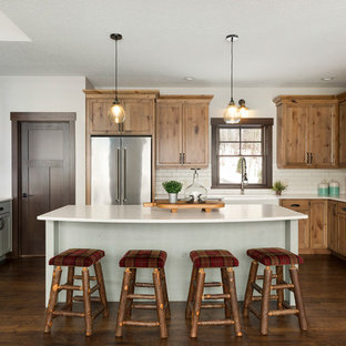 Modelo de cocina en L, rural, con fregadero sobremueble, armarios estilo shaker, puertas de armario de madera oscura, salpicadero blanco, salpicadero de azulejos tipo metro, electrodomésticos de acero inoxidable, suelo de madera oscura, una isla, suelo marrón y encimeras blancas