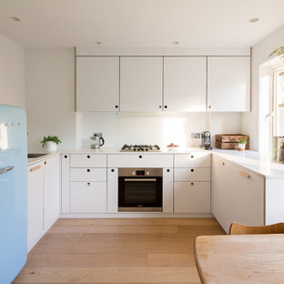 Design ideas for a small scandinavian u-shaped kitchen/diner in London with a submerged sink, flat-panel cabinets, white cabinets, light hardwood flooring, no island, beige floors, white worktops, white splashback, glass sheet splashback and coloured appliances.