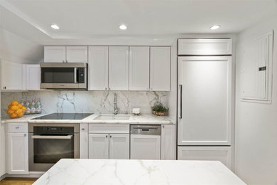 Example of a mid-sized transitional galley light wood floor eat-in kitchen design in Boston with an undermount sink, recessed-panel cabinets, white cabinets, marble countertops, white backsplash, marble backsplash and paneled appliances