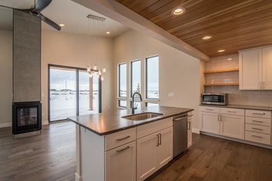 Eat-in kitchen - mid-sized modern l-shaped medium tone wood floor and brown floor eat-in kitchen idea in Other with a single-bowl sink, shaker cabinets, white cabinets, granite countertops, white backsplash, subway tile backsplash, stainless steel appliances and an island