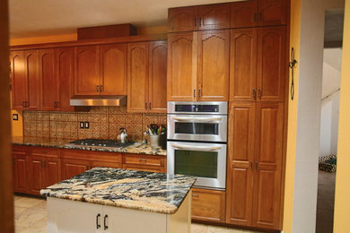 Kitchen pantry - mid-sized southwestern l-shaped travertine floor and beige floor kitchen pantry idea in Albuquerque with raised-panel cabinets, medium tone wood cabinets, glass tile backsplash, stainless steel appliances, an island, granite countertops and brown backsplash